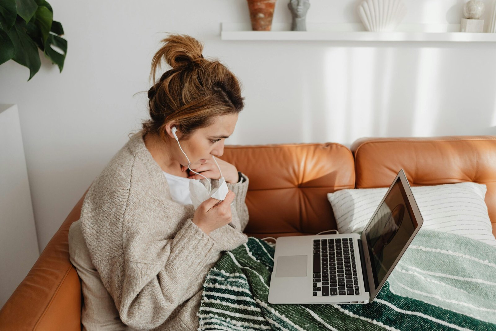 Young woman video chatting on laptop while wrapped in a blanket on a cozy sofa.