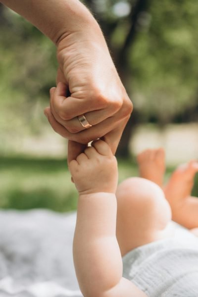 Tender moment of a mother holding her baby's hand outdoors in summer.