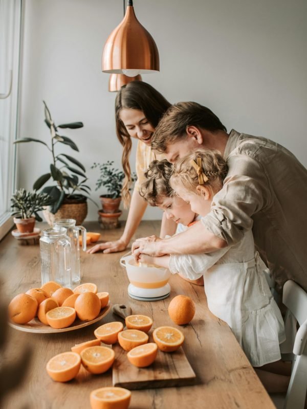 A family enjoys squeezing fresh orange juice together in a cozy kitchen setting filled with natural light.